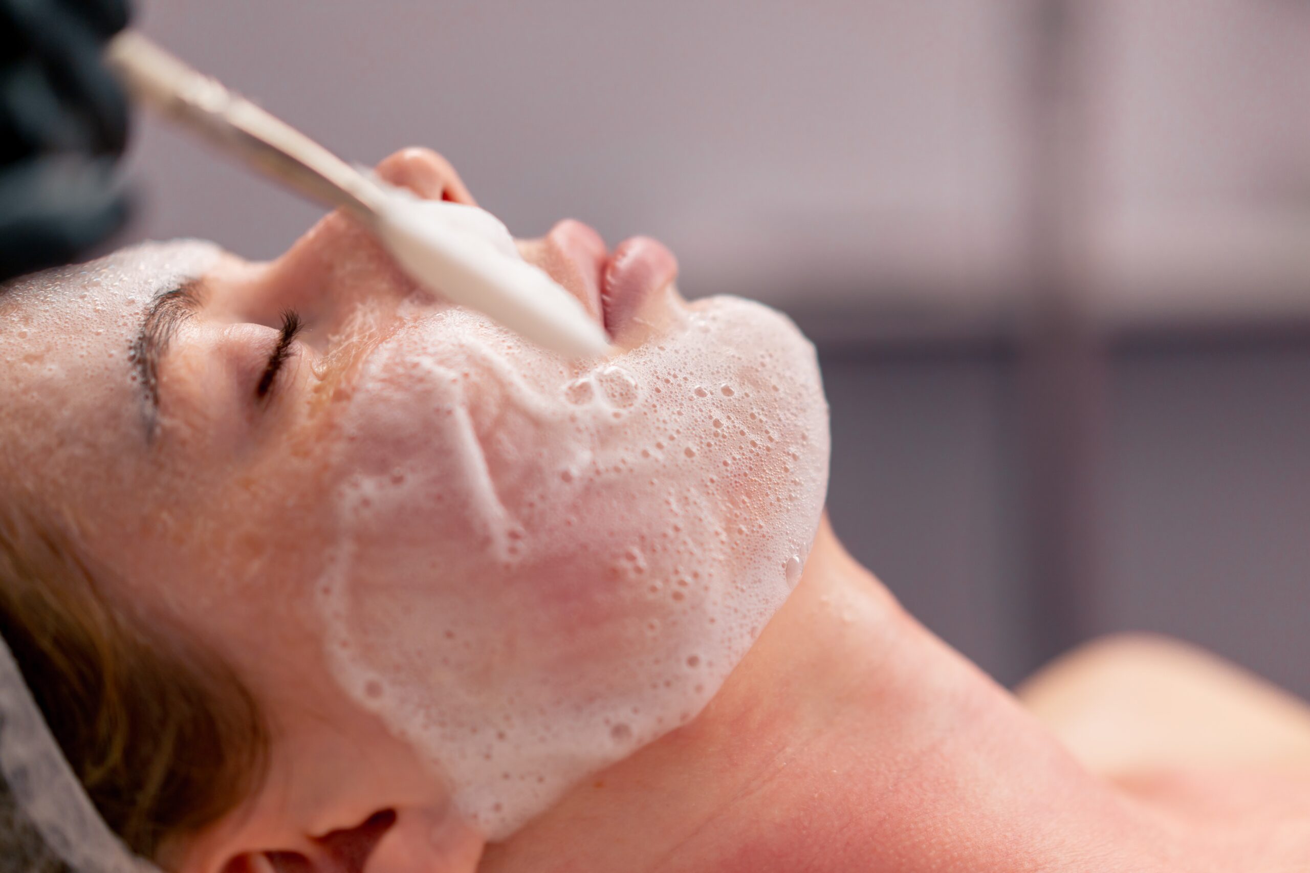 close-up beautician in gloves applies foam with a brush to the client's face takes care of the skin